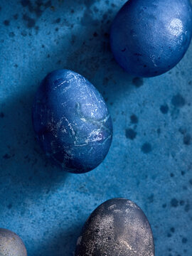 Vibrant blue and dark gray decorative eggs are beautifully arranged on a textured blue surface, evoking a sense of spring and festive celebration