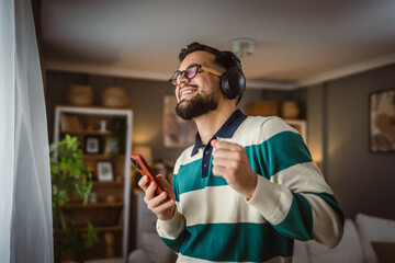 happy man listen music on headphones and sing on cellphone at home