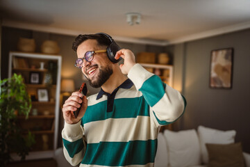 happy man listen music on headphones and sing on cellphone at home