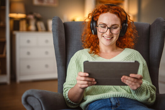 woman sit in the armchair use tablet and listen music on headphones