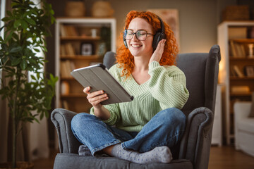 Obraz premium woman sit in the armchair use tablet and listen music on headphones