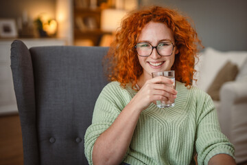 portrait of redhead adult woman drink water and sit in the armchair