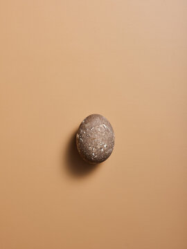 A smooth, oval stone rests against a soft beige surface, showcasing its natural texture and shape. The lighting creates a gentle shadow, enhancing its organic appeal