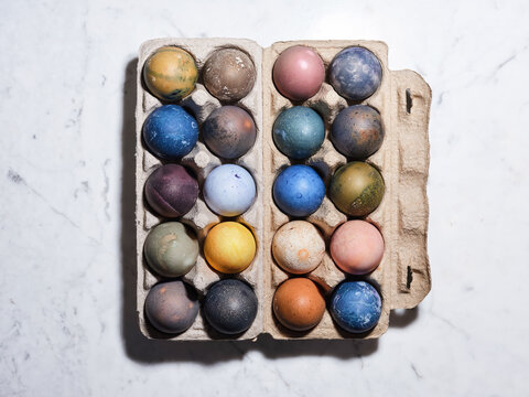 A variety of twenty vibrant, pastel-colored eggs rest in a carton on a marble surface, showcasing the festive spirit of Easter preparations and decoration