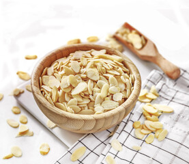 Świeże płatki migdałowe w drewnianej misce na białym tłe © Jolaya