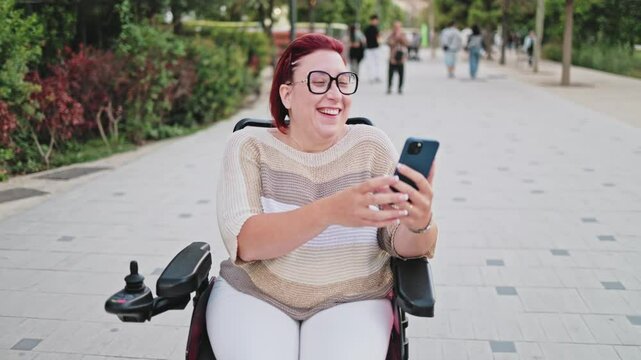 Happy disabled woman using smartphone in electric wheelchair