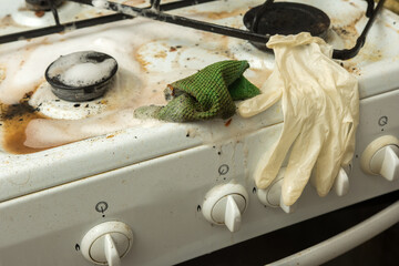 Dirty gas stove with soap foam, sponge, and rubber glove during cleaning process
