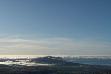 A wall of mist rolls in from the sea towards mountains wrapped in a cloud inversion under a clear...