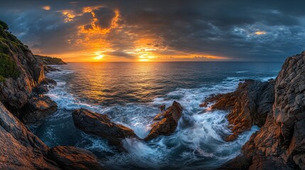 Obraz premium The sun sets beautifully over a rugged coastline, casting vibrant colors across the sky. Waves crash against the rocks, creating a tranquil yet dynamic atmosphere at dusk