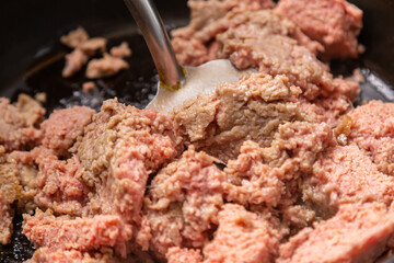 Frozen ground beef in a frying pan with vegetable oil is broken up with a spatula