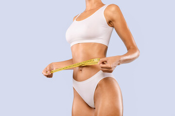 Cropped close up view of half-turned slim woman in white underwear measuring waist with yellow...