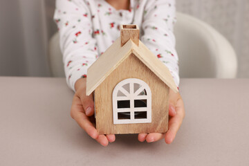 Adoption. Little girl with house figure at beige table, closeup