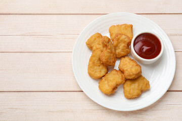 Delicious chicken nuggets and ketchup on wooden table, top view. Space for text