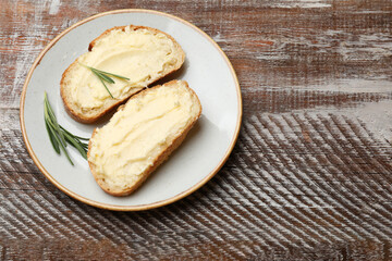 Fresh bread with butter and rosemary on wooden table, top view. Space for text