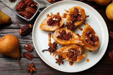 Delicious pears with caramel sauce, pecan nuts and spices on wooden table, flat lay