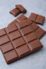 Pieces of delicious milk chocolate on grey table, closeup