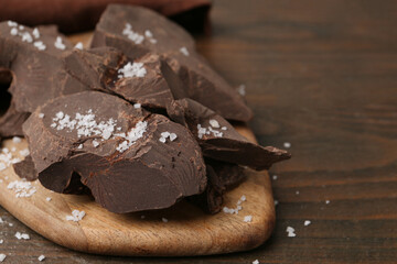 Pieces of chocolate with salt on wooden table, closeup. Space for text