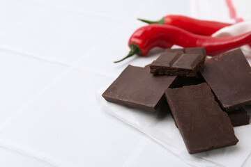 Pieces of chocolate with chili peppers on white table, closeup. Space for text
