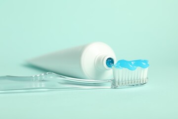 Toothbrush with toothpaste and tube on light blue background, closeup