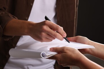 Man signing autograph in notebook on black background, closeup