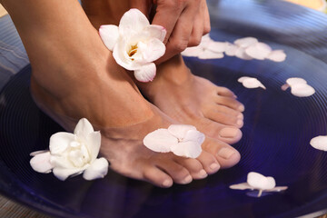 Woman soaking her feet in bowl with water and flowers, closeup. Spa treatment