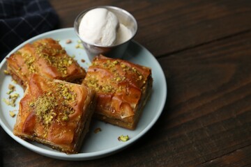 Delicious baklava with crushed nuts and ice cream on wooden table, closeup. Space for text