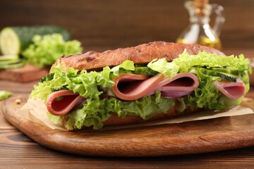 Delicious baguette sandwich with ham on wooden table, closeup