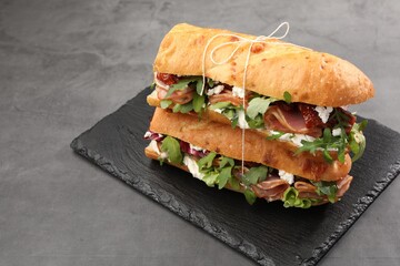 Halves of baguette sandwich with prosciutto and sun dried tomatoes on grey table