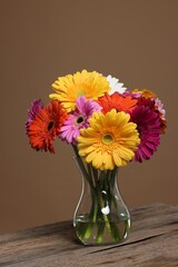 Bouquet of beautiful gerbera flowers in glass vase on wooden table against brown background