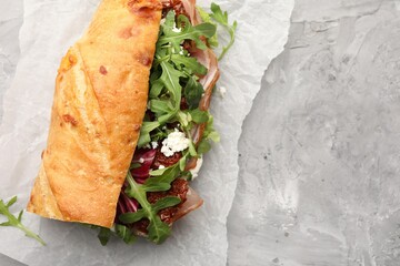 Baguette sandwich with ham and sun dried tomatoes on grey textured table, top view. Space for text