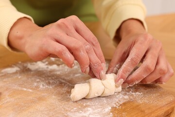 Fototapeta premium Woman making croissant at wooden table, closeup