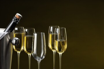 Bottle of sparkling wine in cooler bucket and glasses against brown background, closeup. Space for text