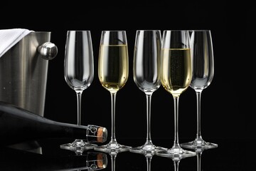 Bottle of sparkling wine, glasses and cooler bucket on black mirror surface