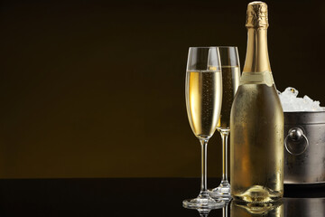 Bottle of sparkling wine, glasses and cooler bucket on black mirror surface. Space for text
