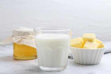 Fresh milk in glass, honey and butter on white marble table, closeup