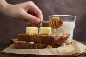 Woman pouring honey onto slices of bread with butter at wooden table, closeup