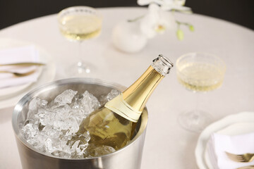 Bottle of sparkling wine in cooler bucket and glasses on light table, closeup