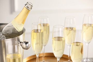 Bottle of sparkling wine in cooler bucket and glasses against light background, closeup
