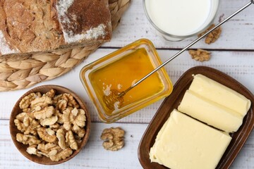 Sweet honey, butter, milk, bread and walnuts on white wooden table, flat lay