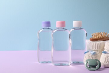 Baby oil in bottles, pacifier, brush and accessories on violet table against light blue background. Space for text