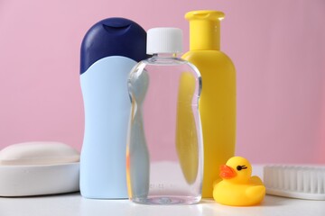 Baby oil and other toiletries on white table against pink background