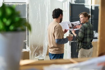 Young couple discussing sketches of new interior for living room while woman holding several papers and looking at her husband
