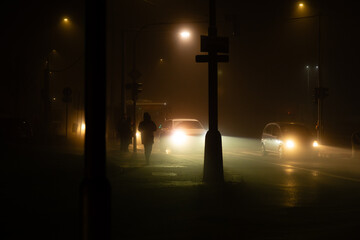 Night intersection with cars, bus and pedestrians illuminated by orange sodium vapour street lamps