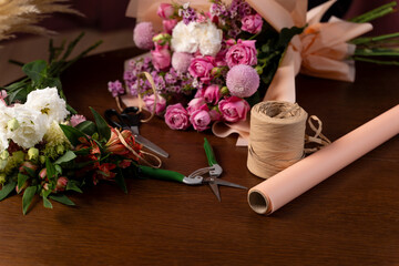 Collecting compositions of bloom mixed flowers in the floral studio. Process of assembling a bouquet. Wrapping bouquets of flowers into craft paper by florist.
