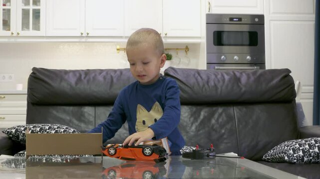 Impatient child unboxing new toy at home. Excited little boy unpacks remote-controlled transformer car.