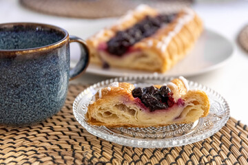 A slice of pie with berry filling on a glass plate and a mug of coffee on a dining table. Photo