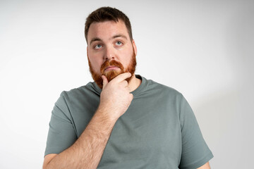Thoughtful male customer thinking hard, looking away at copy space, leaning chin on hand. Handsome young man in casual t-shirt and glasses standing isolated over grey background. Special offer concept