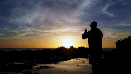 Obraz premium Solo traveler capturing stunning sunset views over the Atlantic Ocean in the Canary Islands, embracing the golden hour's warm light and the breathtaking seascape
