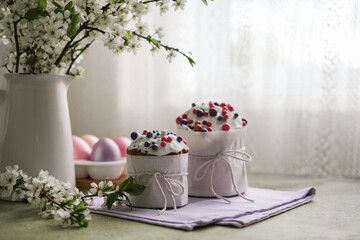 Easter cakes, multi-colored painted eggs and vase of blossoming cherry branches on table by the window
