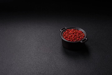 Spice, allspice peas in red or pink color in a bowl on a black concrete background